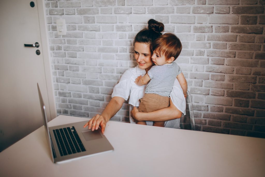Mom holding a child while working and practicing time saving tips for working moms.