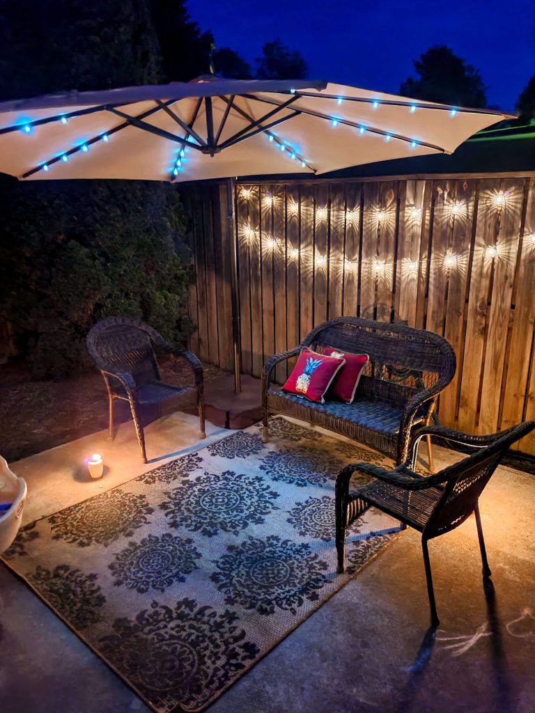 At Home Date Night Ideas for Parents - Head outside and enjoy your patio space like this one pictured with lights, seating, and an outdoor umbrella.