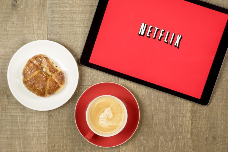 iPad with Netflix on the screen next to a pastry and cup of coffee