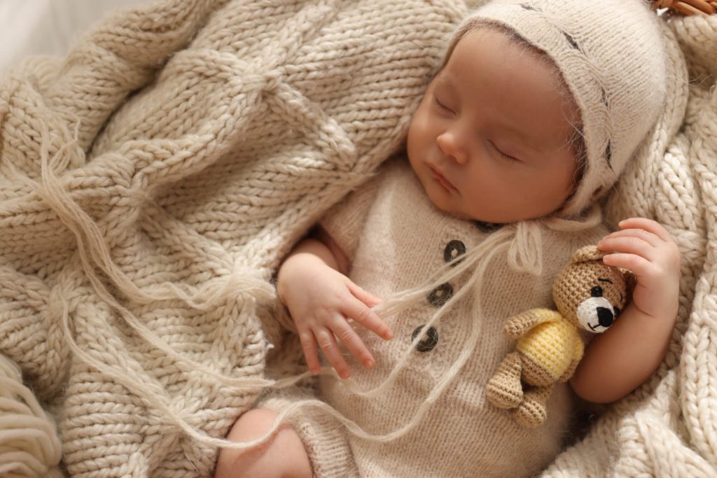 Beautiful baby sleeping in a basket of blankets holding a little teddy bear