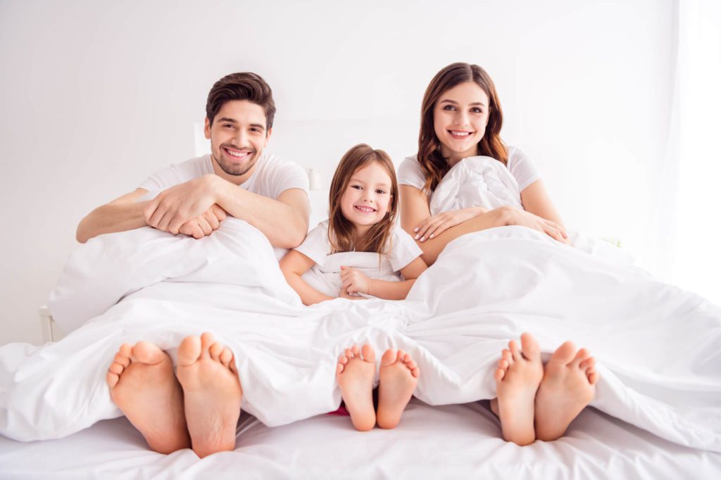 A young family on a bed together on a Sunday morning self care day.