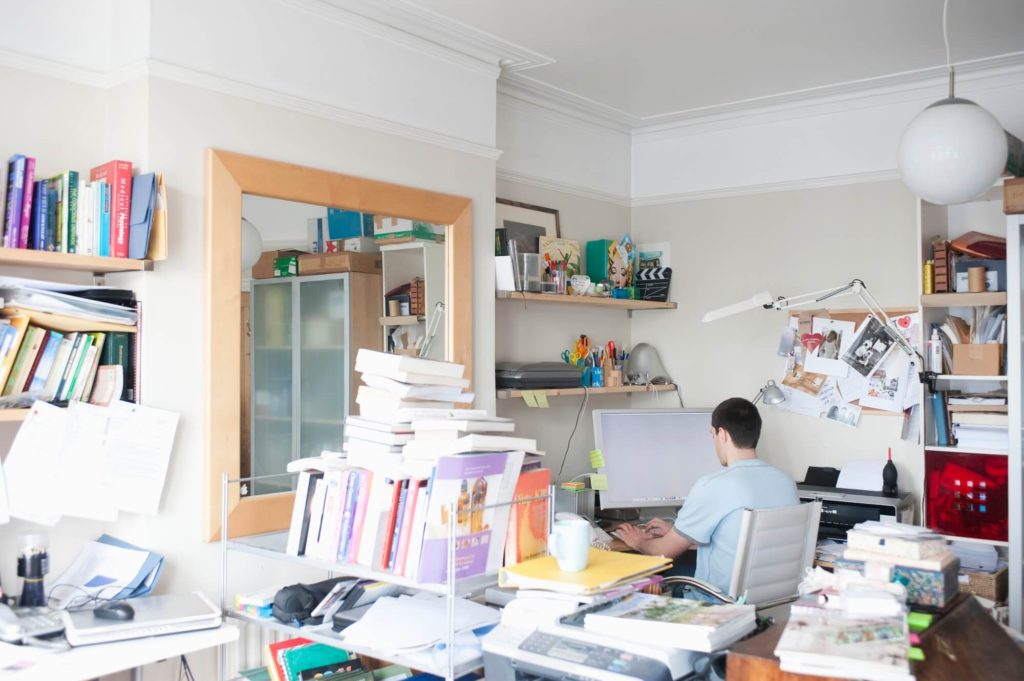 Man working in an office that is filled with clutter.