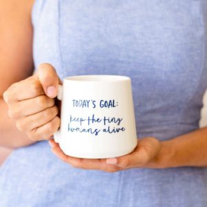 A woman holding a mug that says, Today's Goal: Keep the tiny humans alive.