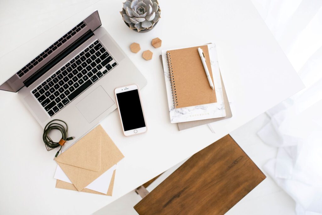Flatlay of a computer, paper, phone, notebook, pen and other accessories on a white desktop