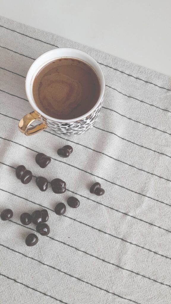 A cup of coffee on a towel with coffee beans spilled to one side.