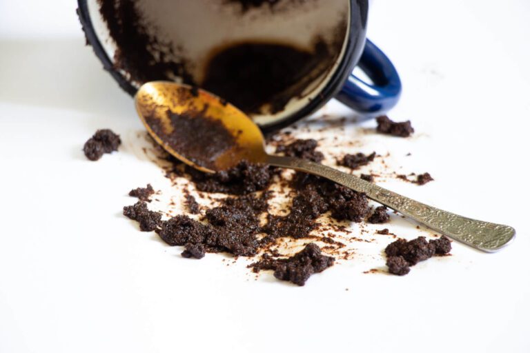 Used coffee grounds falling out of a mug with a spoon.