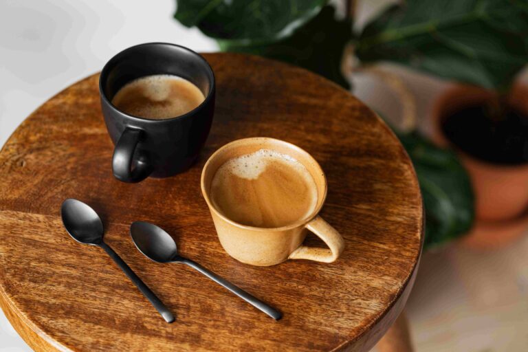 Two cups of coffee on a wood table top with two spoons.