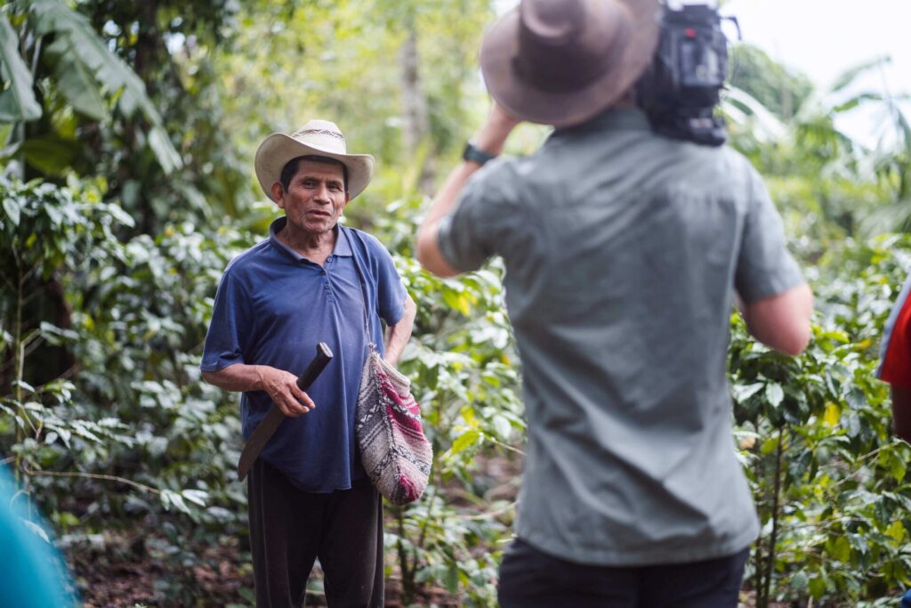 A coffee farmer being filmed by a man for a coffee documentary.