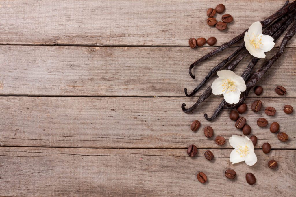 Vanilla beans and coffee beans on a wood-like background.