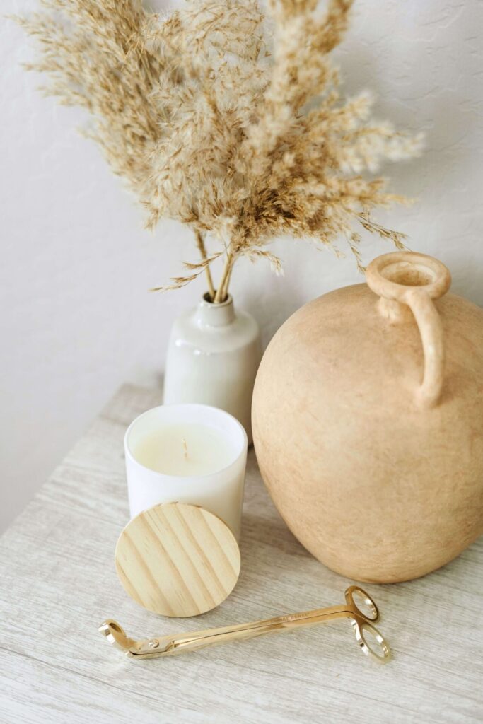 An urn next to a candle on a table top with a vase of dried cotton.