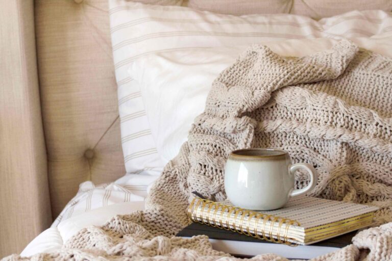 A coffee mug on a journal on top of a bed with blankets.