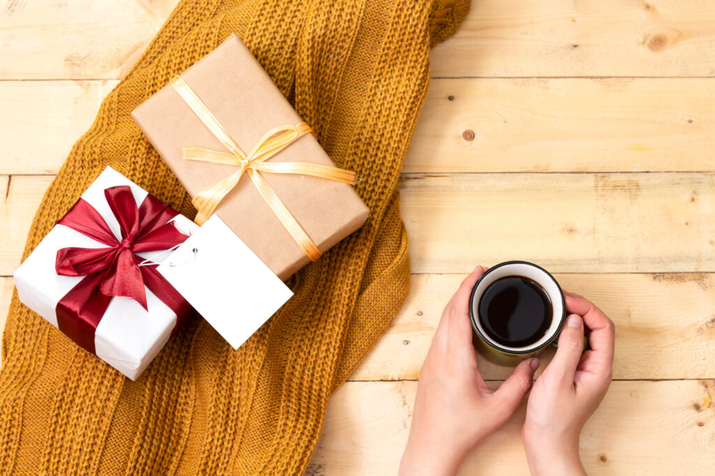 A mom holding a cup of coffee next to some presents.