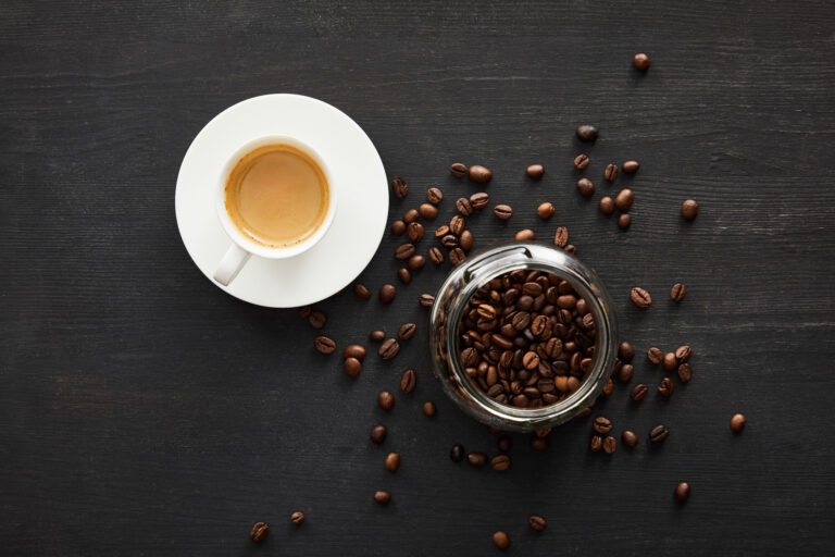 A cup of coffee next to coffee beans.