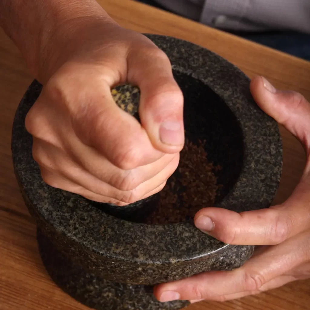 A person grinding flaxseed coffee with a mortar and pestle.