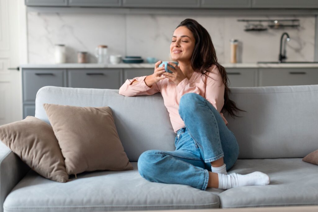A woman drinking a cup of coffee on a couch.