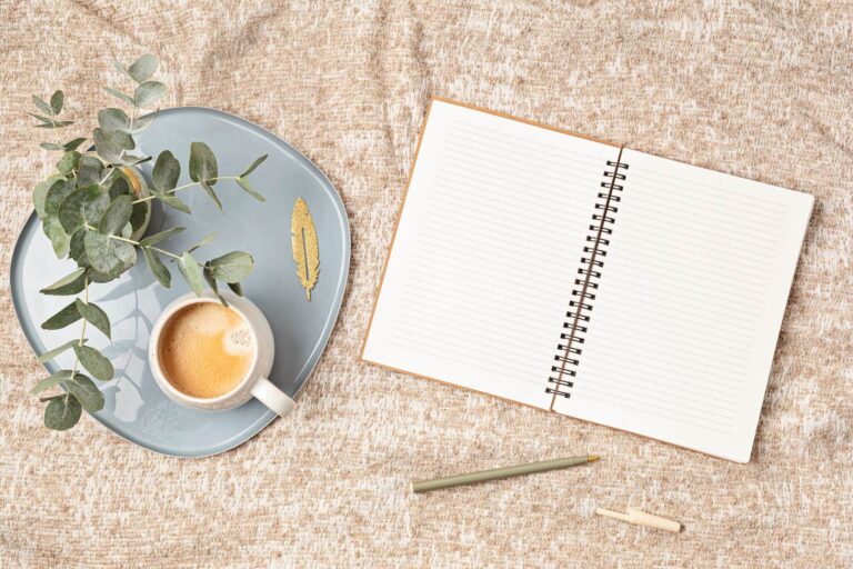 A blank journal on a flat surface next to a cup of coffee.