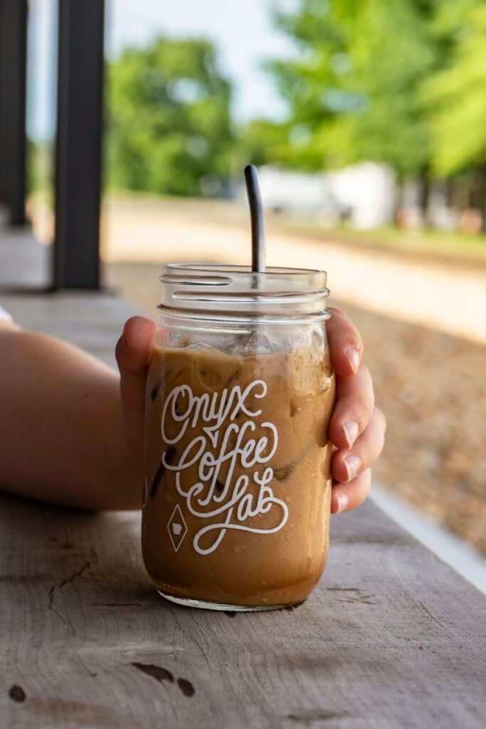 A person holding a clear glass of iced coffee that says Onyx Coffee Lab.